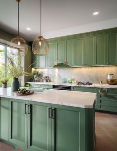 a large kitchen with green cabinets and marble counter tops, along with an island in the middle