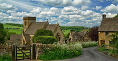 an old village with stone buildings and lush green fields under a blue sky filled with clouds