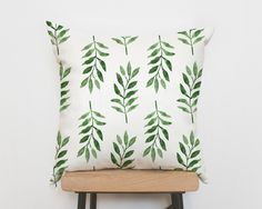 a white pillow with green leaves on it sitting on a chair next to a wall