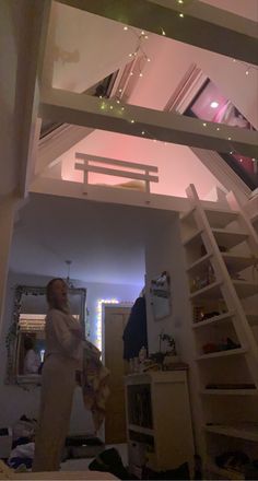 a woman is standing in the middle of a room with stairs leading up to her bed