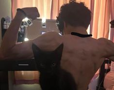 a shirtless man holding a black cat in front of his back