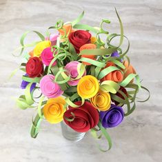 a bouquet of colorful paper flowers in a metal vase on a marble surface with green ribbon