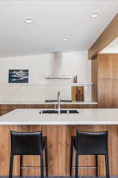 two black chairs are sitting in front of the kitchen counter and island with an oven