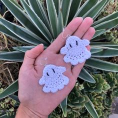 a hand holding two small crocheted sheeps in front of a succulent plant