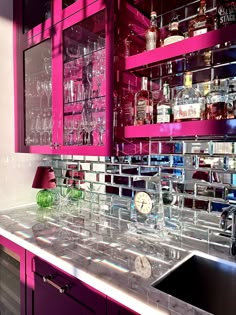 a kitchen with pink cabinets and shelves filled with liquor bottles on top of it's counter tops