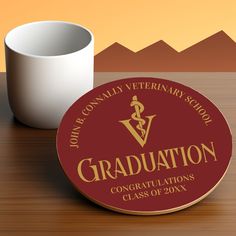 a coffee cup sitting on top of a wooden table next to a graduation plaque that says, john b conley veterinary school