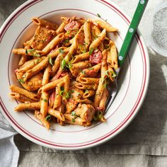 a white bowl filled with pasta and meat on top of a table next to a fork