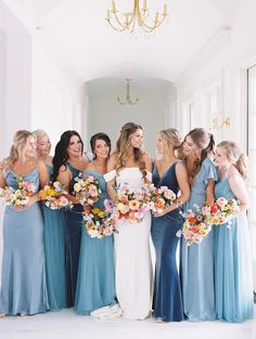 a group of women standing next to each other holding bouquets in front of a chandelier