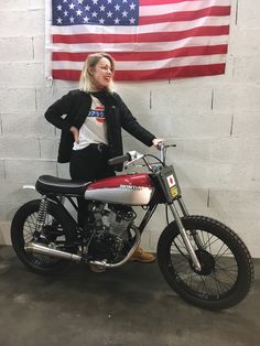 a woman standing next to a red and white motorcycle in front of an american flag