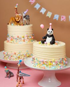 two tiered birthday cake with animals and balloons on the top, next to a pink tablecloth