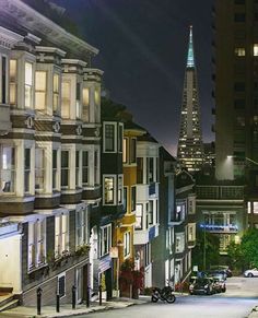 a city street at night with cars parked on the side and tall buildings in the background