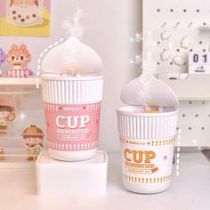 two cups sitting next to each other on top of a white table with toys in the background