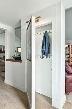 an open closet with clothes hanging on the door and a couch in the back ground