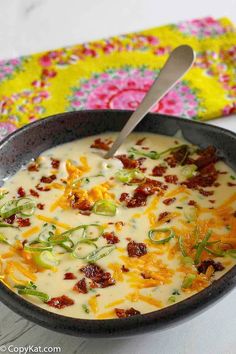 a bowl of soup with cheese and bacon in it next to a colorful place mat