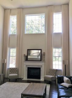 a living room filled with furniture and a fire place in front of two large windows