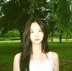 a young woman standing in front of a lush green park filled with lots of trees