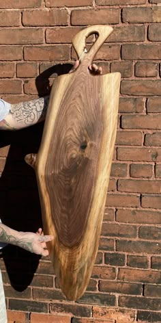 a man holding a large wooden object in front of a brick wall with his hands on it