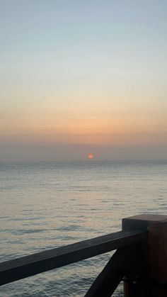 the sun is setting over the ocean from a pier