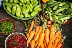 several bowls filled with carrots, cucumbers and other veggies next to each other