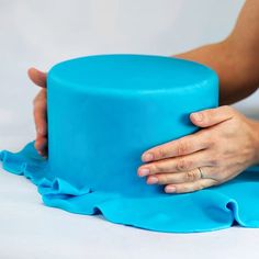 a person holding onto a blue cake on top of a table