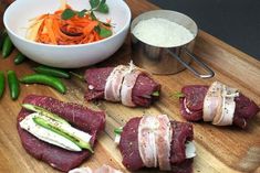 some meats and vegetables on a cutting board next to a bowl of carrots