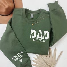 a green sweatshirt with the words dad est 2020 printed on it next to a hat