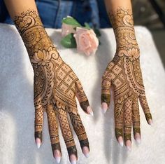 two hands with henna tattoos on them sitting next to a pink rose and another person's hand