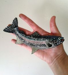 a hand holding a small toy fish in it's left palm on a white surface