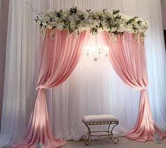 a white and pink wedding arch with flowers on it's side, hanging from the ceiling