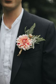 a man wearing a black suit and white shirt with a flower on his lapel