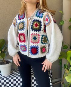 a woman standing in front of a potted plant wearing a white sweater and black pants