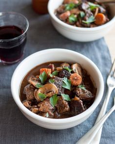 two bowls filled with stew next to a glass of wine