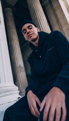 a young man sitting on the steps of an old building with columns and pillars behind him