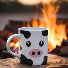 a coffee mug with a cow face on it sitting in front of a fire pit