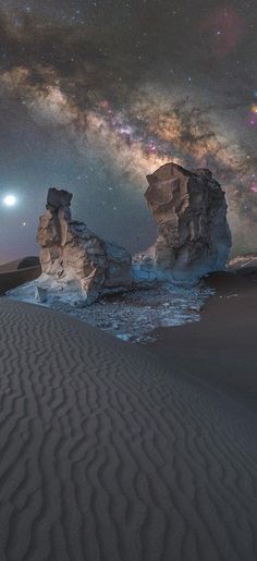 the night sky is filled with stars and clouds, while two large rocks are in the foreground