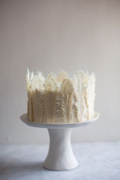 a cake with white frosting and feathers on top is sitting on a plate in front of a wall