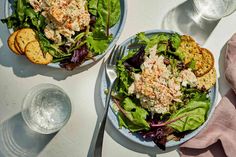 two plates filled with salad and crackers on top of a white tablecloth next to silverware