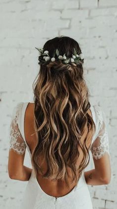 a woman with long hair wearing a white dress and flowers in her hair, standing against a brick wall