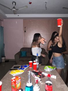 two women standing around a table with drinks and condiments on top of it