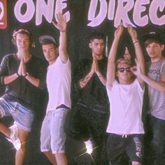 a group of young men standing next to each other in front of a one direction sign