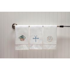 three kitchen towels hanging on a towel rack in front of a white wall with dragonflies and flowers