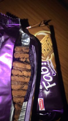 two bags of cookies sitting next to each other on a wooden table with a purple bag