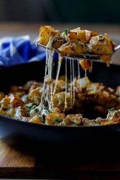 a spoon full of food being lifted from a skillet with cheese and herbs on it