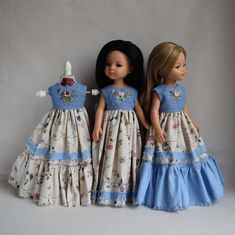 two dolls are standing next to each other on a white surface with grey background and one is wearing a blue dress