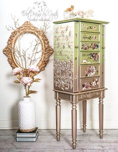 an ornate wooden jewelry cabinet next to a mirror and vase with flowers in it on the floor