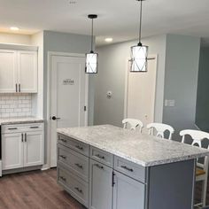 a kitchen with white cabinets and gray counter tops, an island in the middle is surrounded by chairs