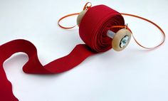 a roll of red ribbon sitting on top of a white table next to a pair of scissors