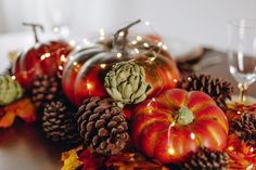 an arrangement of pumpkins and pine cones on a table with lights in the background