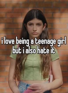 a girl with long hair and green shirt standing in front of a brick wall