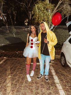 a man and woman dressed in costumes standing next to each other near a fence with balloons